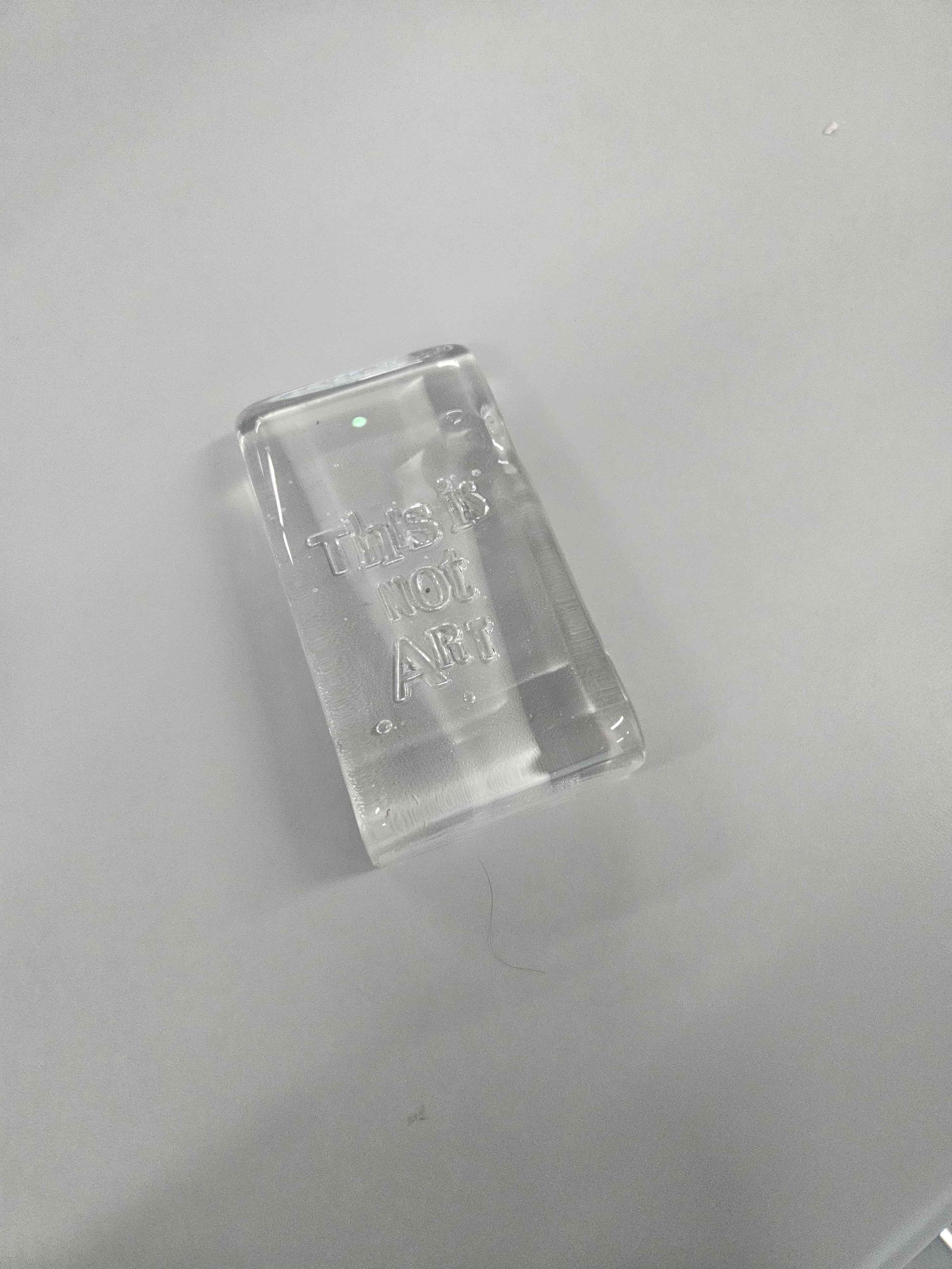 This object material is a piece of glass with indented text which says, 'this is not art'. It is a clear glass with a smooth texture on all sides except for the back which is slightly rough smooth texture. This is a refined object, as intensive labour was put into creating a smooth glass with text. It is not a pliable object as the object can easily shatter. 
      This object is used for construction (windows), dinnerware and artworks just like this object.